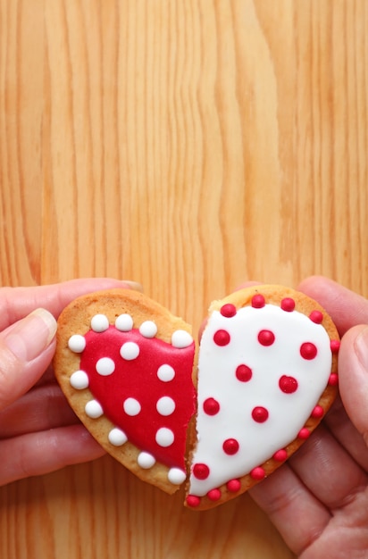 De parenhanden die twee halve hartvormige koekjes houden hechten zich vast op houten achtergrond