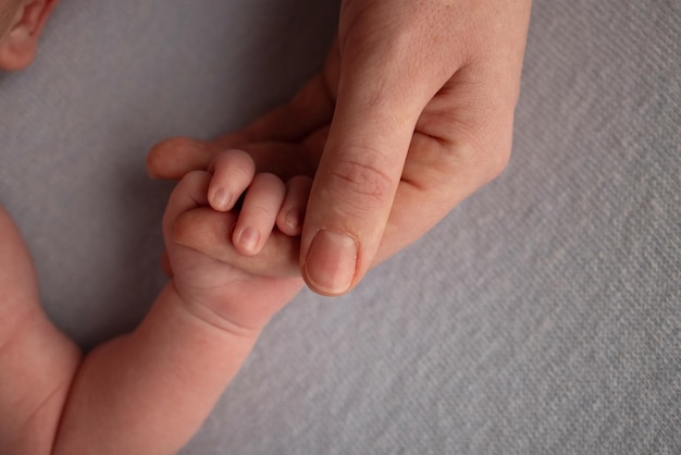 De pasgeboren baby heeft na de geboorte een stevige grip op de vinger van de ouder. Close-up handje van kind en palm van moeder en vader. Ouderschap, kinderopvang en gezondheidszorg concept.