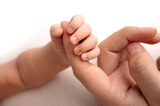 De pasgeboren baby in een witte sluiting heeft na de geboorte een stevige grip op de vinger van de ouder. Close-up handje van kind en palm van moeder en vader. Ouderschap, kinderopvang en gezondheidszorg concept.