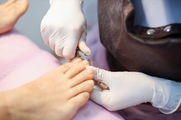 De pedicuremeester houdt een nagelknipper in zijn handen en snijdt de teennagels af