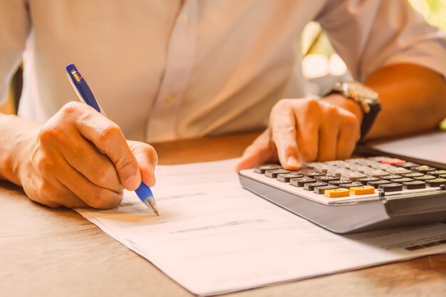 De pen van de zakenmanholding op document aan het analyseren van boekhouding met calculator.