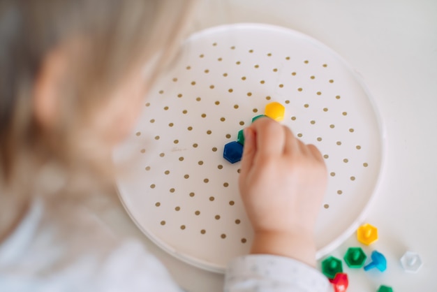 De peuter maakt een figuur van een plastic mozaïek.