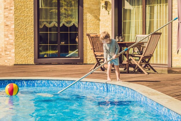 De peuterjongen maakt het zwembad schoon en trekt de bal uit het zwembad. Zwembadreiniger Concept