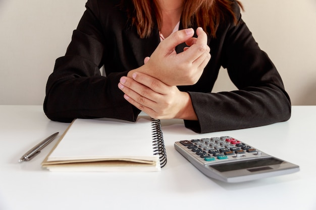 Foto de pijn van onderneemsterhanden op het syndroom van het bureaubureau met notitieboekje en calculator.