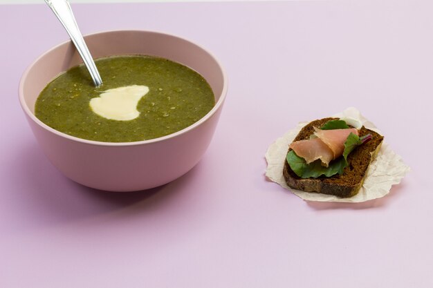 De plantaardige soep van de broccolipuree in roze kom en sandwiche op bureau.