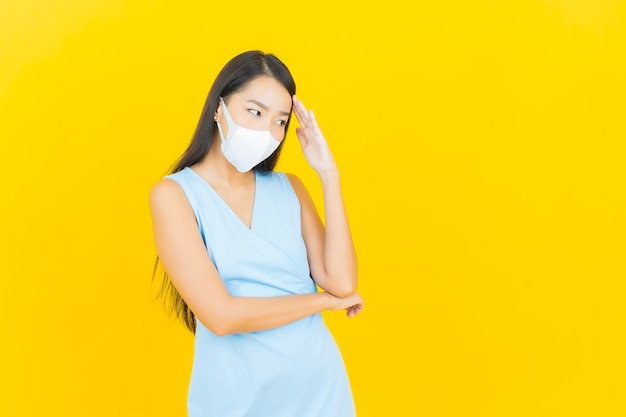 De portret mooie jonge aziatische vrouw met masker voor beschermt covid19 of virus op gele kleurenmuur