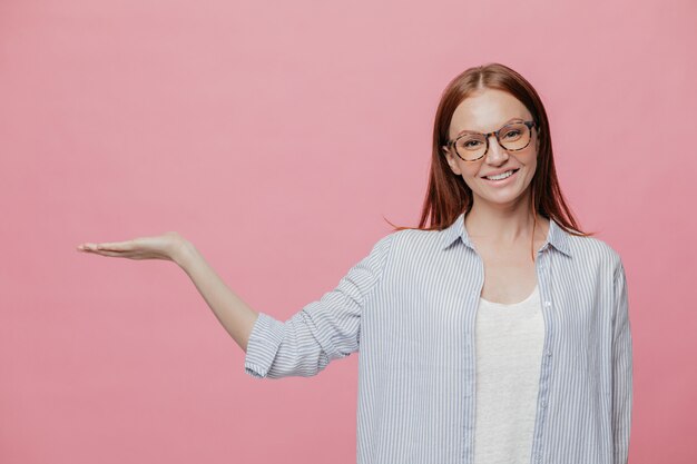 De positieve jonge glimlachende vrouw heft hand op, beweert iets te houden