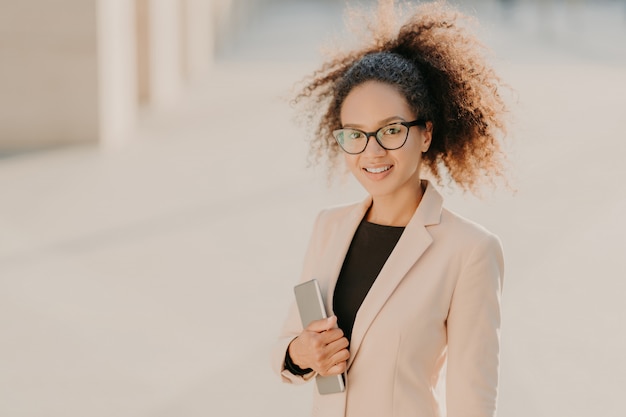 De positieve schitterende amerikaanse onderneemster van afro wandelt openlucht met touchpad