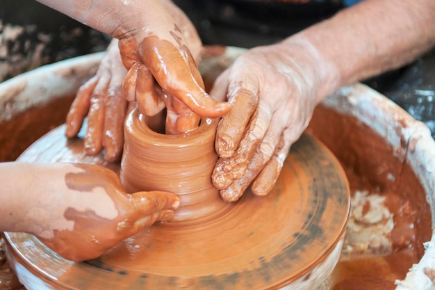 De pottenbakker maakt aardewerkschotels op het wiel van de pottenbakker de beeldhouwer in de werkplaats maakt een kleiproductclose-up handen van de pottenbakker