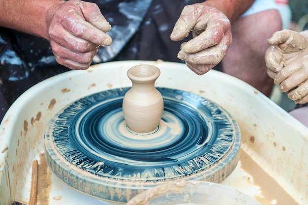 De pottenbakker maakt aardewerkschotels op het wiel van de pottenbakker De beeldhouwer in de werkplaats maakt een kleiproductclose-up Handen van de pottenbakker