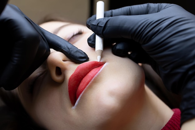 De procedure van permanente liptatoeëring de meester houdt de punt van de lippen met zijn vinger vast en brengt de contour aan met een wit potlood