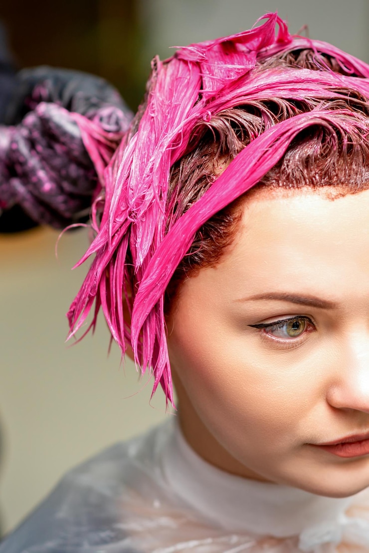 Foto de professionele kapper gebruikt een borstel om de roze kleurstof op het haar aan te brengen. haarkleuring concept.