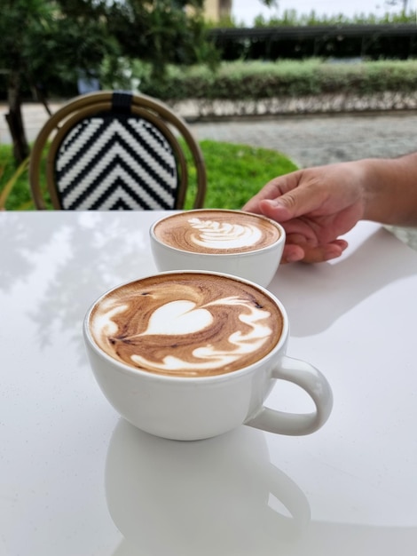 De rechterhand houdt een van de twee kopjes hete latte art-koffie vast terwijl hij op een witte tafel staat