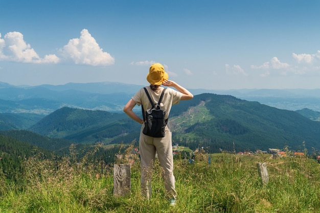 De reiziger in hoed en rugzak die in de natuur rust Een toeristisch meisje kijkt naar panorama van bergen