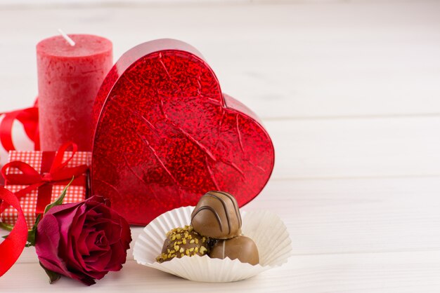 De rode achtergrond van de valentijnskaartendag met rode rozen en chocolade op een witte houten lijst.