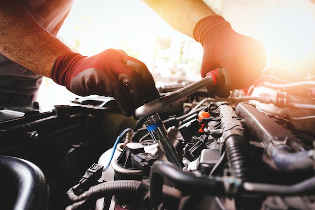 De rode gehandschoende hand van de automonteur maakt de bout vast met de dopsleutel om het zonlicht van de voertuigmotor op de achtergrond te bevestigen