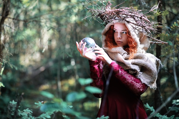 De roodharige heks houdt een ritueel met een kristallen bol in het bos