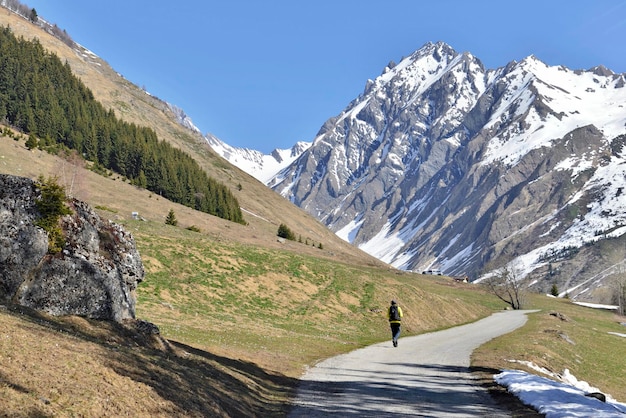 De rotsachtige berg sneeuwde nog in de lente aan het eind van een weg waar het silhouet van een wandelaar in de Franse Alpen loopt