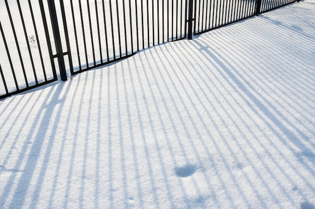 De schaduw van een metalen hek valt op een zonnige dag op schone sneeuw