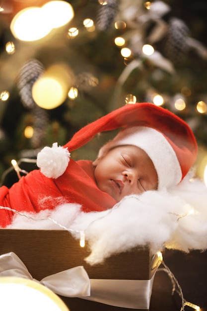 De schattige pasgeboren baby die de hoed van de Kerstman draagt slaapt in de doos van de Kerstmisgift