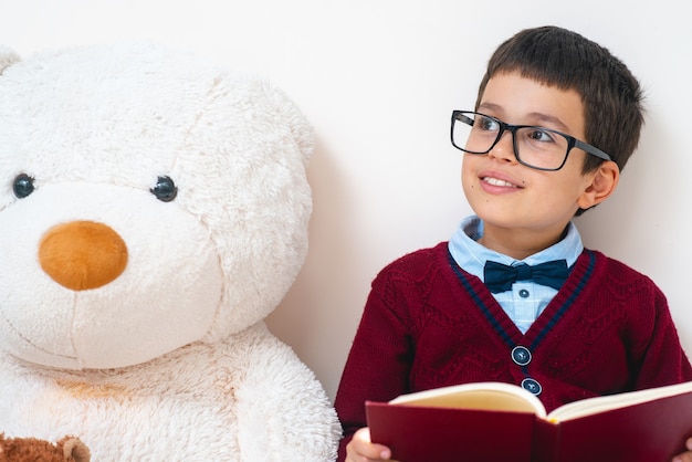 De schooljongen in trui en bril zit naast een grote teddybeer met een opengeslagen boek in zijn handen
