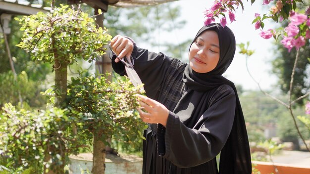 De schoonheid in hijab snijdt de bladeren in de tuin