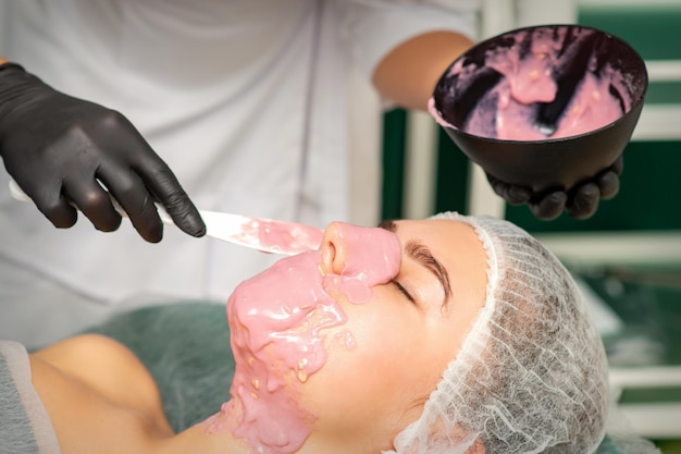 De schoonheidsspecialist die een alginaatmasker toepast op het gezicht van een jonge vrouw in een schoonheidssalon.