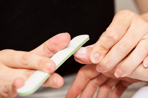 De schoonheidsspecialist poetst de nagels van de klant voordat hij nagellak aanbrengt