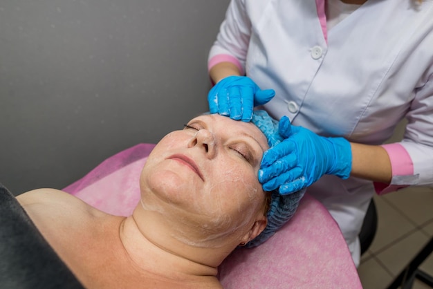 De schoonheidsspecialiste masseert het gezicht en het hoofd van een volwassen vrouw die op een massagetafel ligt. Het concept van cosmetologie, massage spa-procedures.