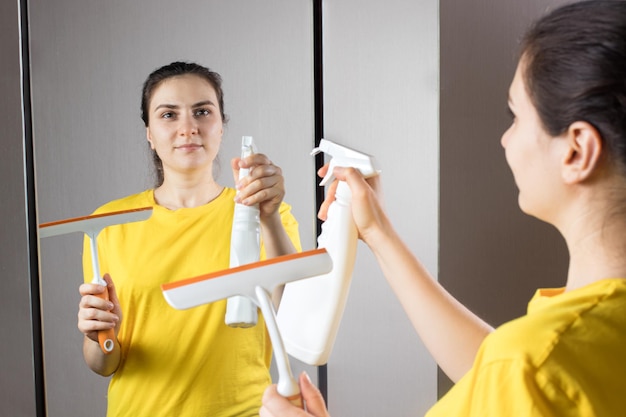 De schoonmaakster maakt de spiegel schoon met een waterdispenser en glazenwasser