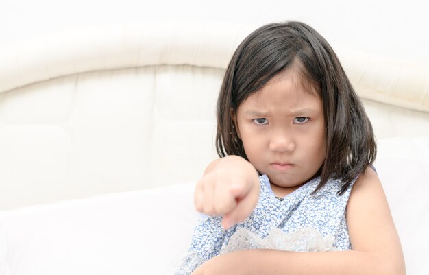 De schuld, beschuldiging. Portret boos meisje wijzende vinger naar iemand ontevreden op bed. Negatief mens