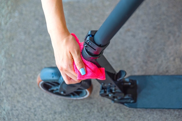 De scooter schoonmaken of wassen. Verzorging van elektrische scooters. Een vrouw veegt een scooter af met een doek na het wassen met water. Plaats voor tekst.