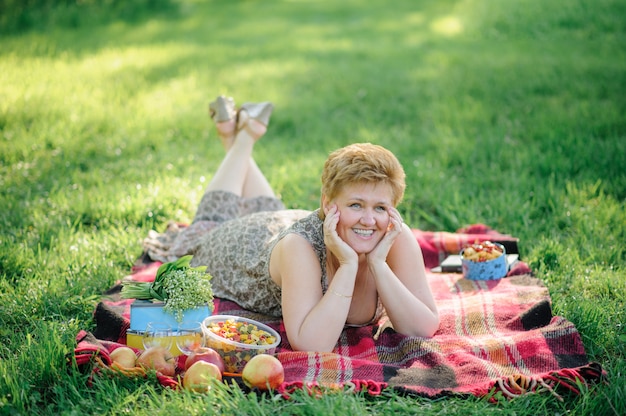 De senior vrouw ligt buik op een plaid en poseert voor de camera in het park op de natuur.