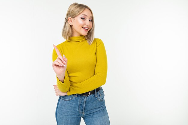 De sexy blondedame in strakke citroenblouse en jeans waarschuwt met haar handen op een witte achtergrond