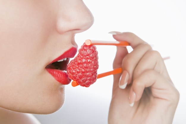 Foto de sexy vrouw eet een framboos aan stokjes en houdt hem bij de lippen