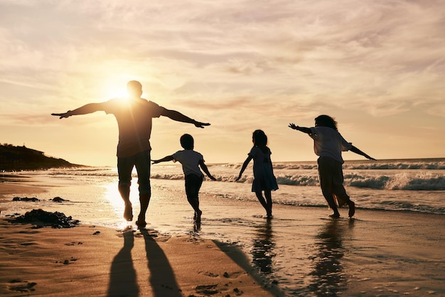 De silhouetfamilie loopt op het strand en achteraanzicht met oceaangolven zonsondergang en binding in de natuur Energieactie mensen buiten op tropische vakantie en vrijheid reizen met vertrouwen en liefde