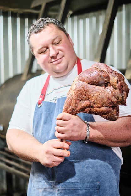 De slager houdt een met marinade gekruide lamsbout voor een grote roker