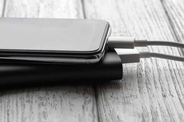 De smartphone laadt op vanaf een externe powerbank met kabel op een grijze houten achtergrond