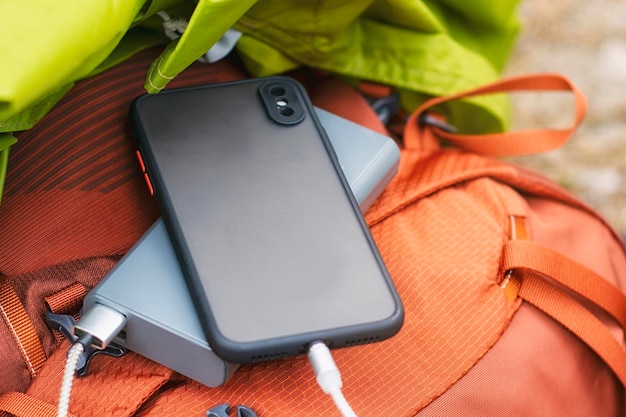 De smartphone wordt opgeladen met een draagbare oplader Powerbank met een mobiele telefoon op een slaapzak met een rugzak