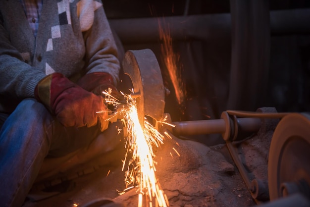 de smid die metalen producten polijst en vonken maakt terwijl hij een slijpmachine gebruikt in zijn traditionele werkplaats