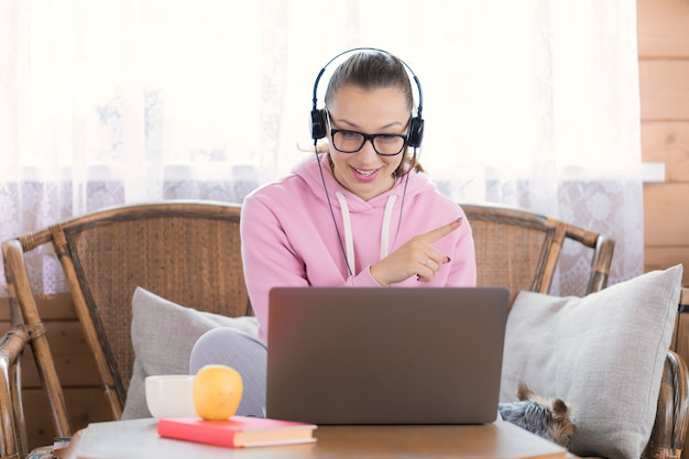 De smileyvrouw in hoofdtelefoons werkt op afstand met laptop computer bij landhuis