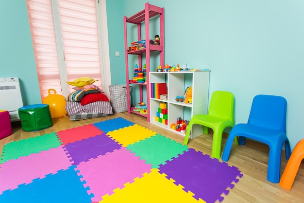 De speelkamer met diverse kasten zachte kussens en gekleurde stoelen Er ligt een kleurig tapijt op de vloer