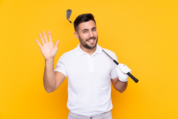 De spelermens van de golfspeler over het geïsoleerde gele muur groeten met hand met gelukkige uitdrukking