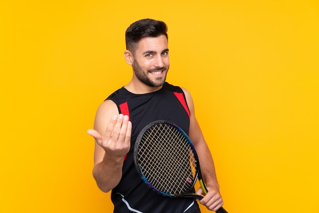 De spelermens van het tennis over geïsoleerde gele muur die met hand uitnodigt te komen. Blij dat je bent gekomen
