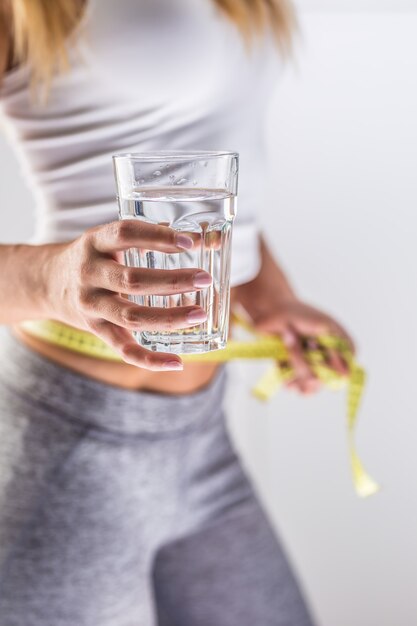 De sportfiguur van een aantrekkelijke vrouw die een beker van zuiver mineraalwater vasthoudt en meetlint.