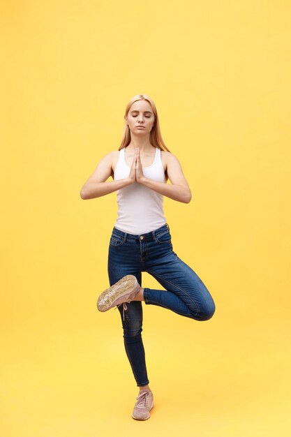 De sportieve aantrekkelijke jonge vrouw in witte sportkleding die oefening voor stekel doen, stelt Vrikshasana