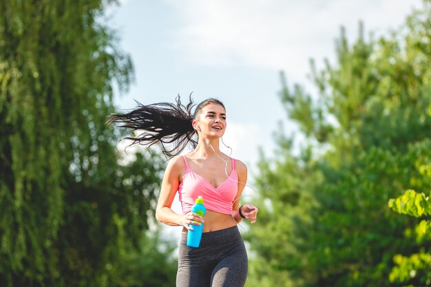 De sportvrouw die buiten met een fles rent