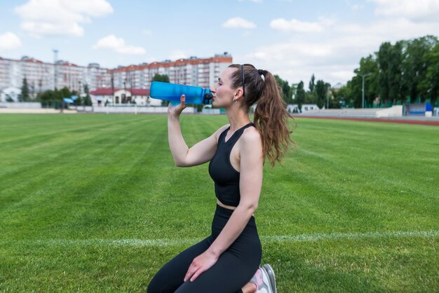 De sportvrouw drinkt water in het stadion Buitentraining