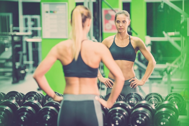 De sportvrouw staat voor de spiegel in de sportschool