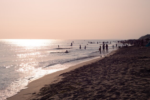 De sprankelende zee bij zonsondergang met silhouetten van rustende mensen. Reizen en toerisme.